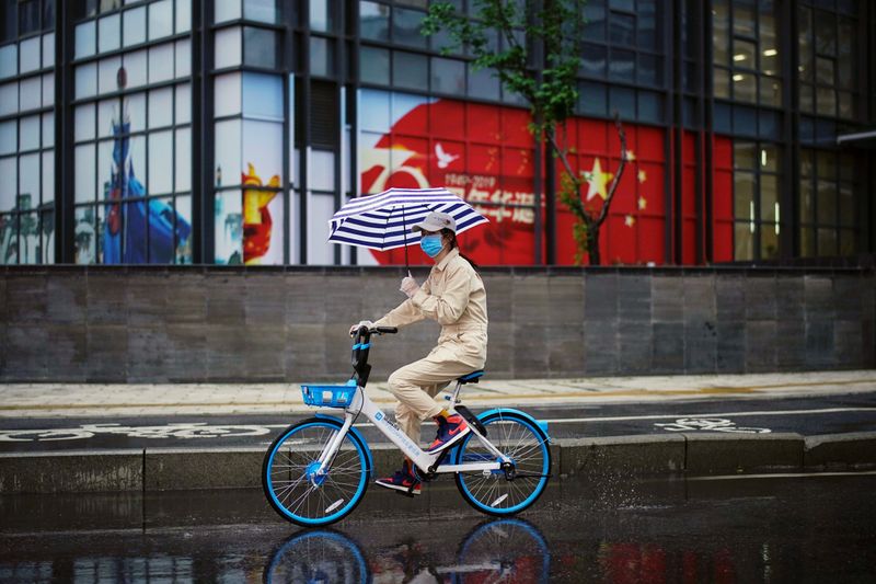 Woman rides a shared bicycle past an image of the Chinese flag in Wuhan