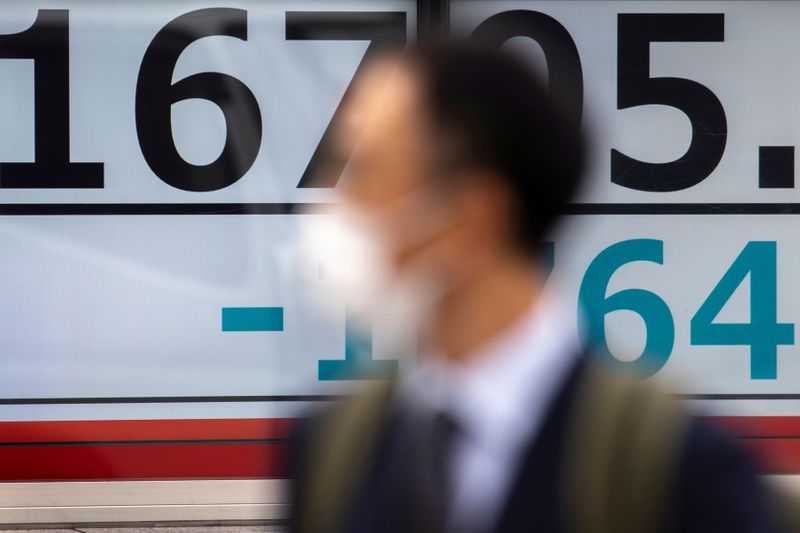 A man wearing a protective face mask walks past a screen showing Nikkei index outside a brokerage in Tokyo