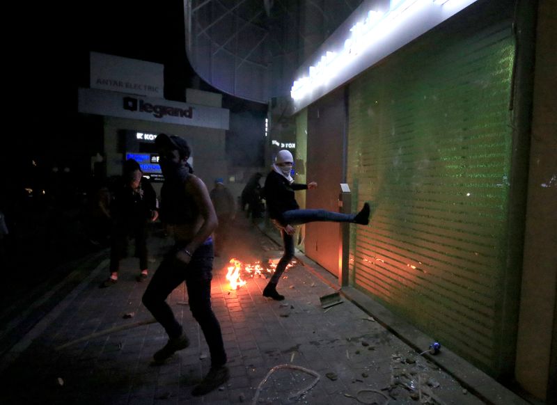 A demonstrator smashes a window of a bank during a protest against growing economic hardship in Sidon