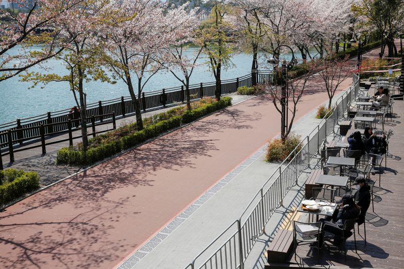 People enjoy the view while practicing social distancing during the global spread of the coronavirus disease (COVID-19), at a cafe near a cherry blossom trees street Seokchon Lake park, in Seoul