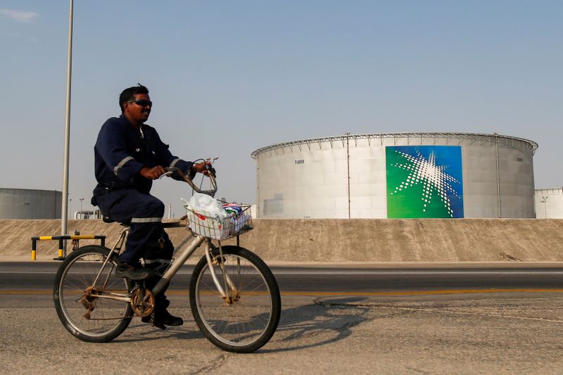 An employee rides a bicycle next to oil tanks at Saudi Aramco oil facility in Abqaiq