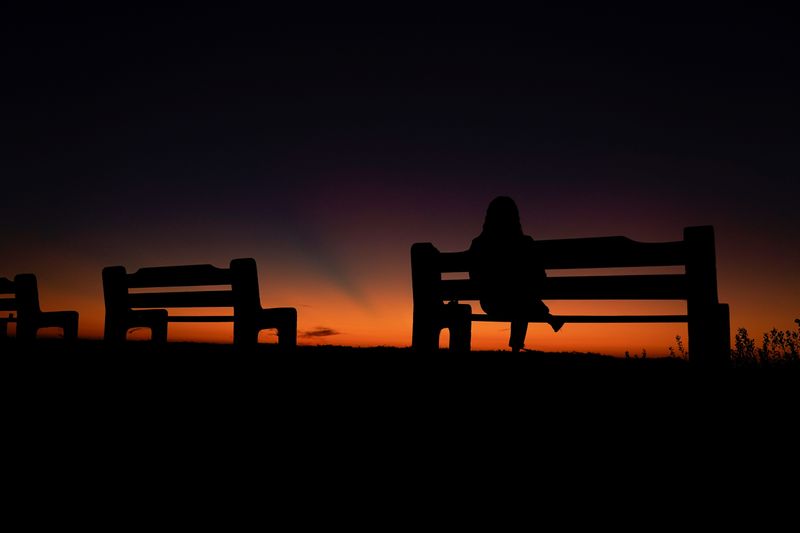 A women sits alone on a park bench watching the sky after sun set in Encinitas, California