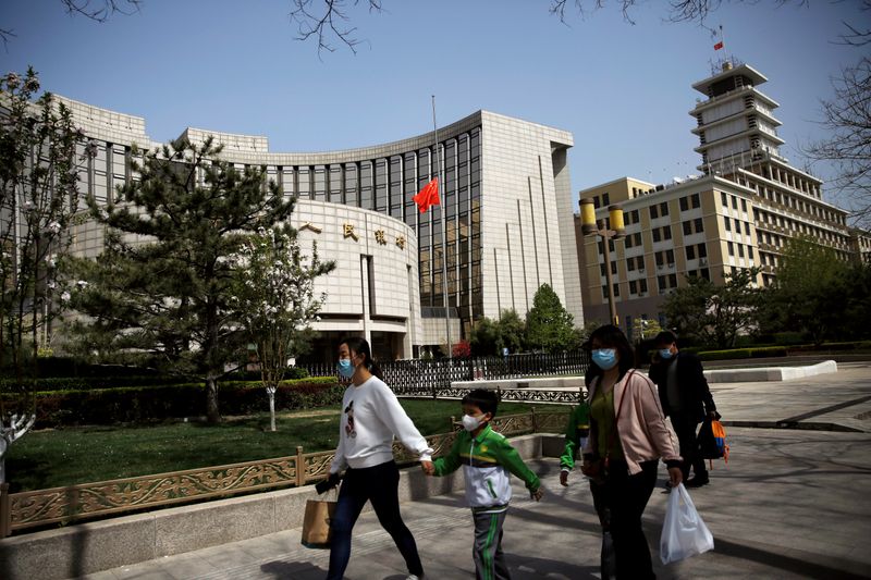 FILE PHOTO: People wearing face masks walk past the headquarters of PBOC, where the Chinese national flag flies at half mast