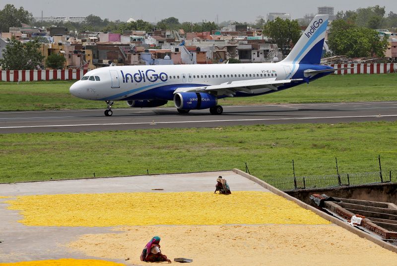 FILE PHOTO: Women spread fryums for drying on a rooftop as an IndiGo Airlines Airbus A320 aircraft moves on the runway after landing at the Sardar Vallabhbhai Patel international airport in Ahmedabad