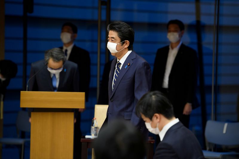 FILE PHOTO: Japan's Prime Minister Shinzo Abe walks wearing a face protective mask during a news conference in Tokyo