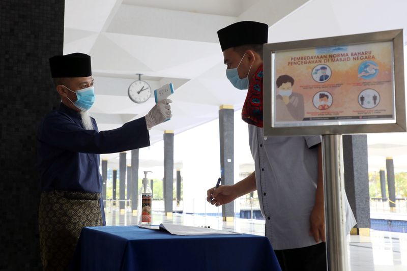 A worker takes the temperature of a man at the National Mosque entrance as Malaysia eases a ban on mass prayers in mosques, amid the coronavirus disease (COVID-19) outbreak, in Kuala Lumpur