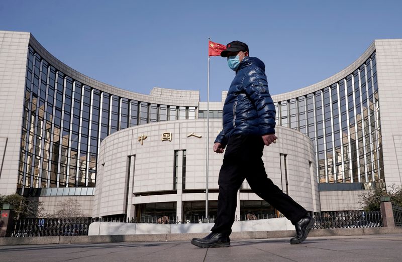 FILE PHOTO: Man wearing a mask walks past the headquarters of the People's Bank of China, the central bank, in Beijing, China