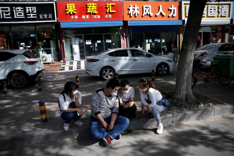 Zhang Ruirui, Zhang Jianpeng, Guo Shengming and Zhang Yanyan sit by a street outside recruiting agencies as they browse job information on a mobile phone, in a suburb of Beijing
