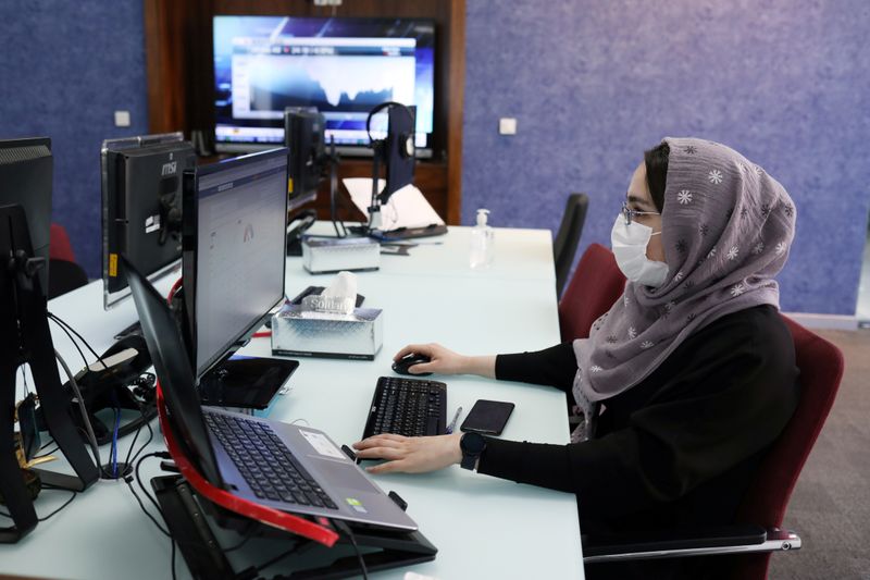 FILE PHOTO: An employee of a stock brokerage firm wearing a protective face mask monitors the stock prices on her computer, following the outbreak of the coronavirus disease (COVID-19), at the brokerage house in Tehran