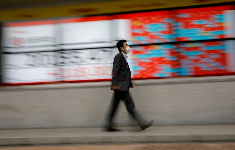 FILE PHOTO: A man wearing a protective face mask, following the coronavirus disease (COVID-19) outbreak, walks in front of a stock quotation board outside a brokerage in Tokyo