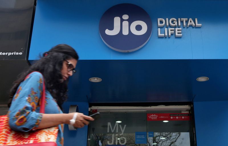FILE PHOTO: A woman checks her mobile phone as she walks past a mobile store of Reliance Industries' Jio telecoms unit in Mumbai