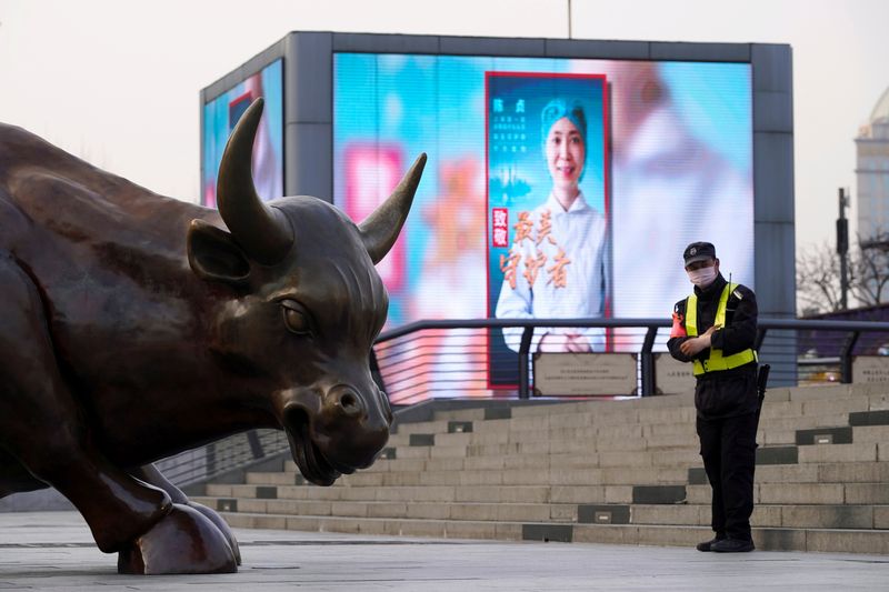 FILE PHOTO: Security guard wearing a face mask stands near the Bund Financial Bull statue and a display showing an image of a medical worker on The Bund in Shanghai