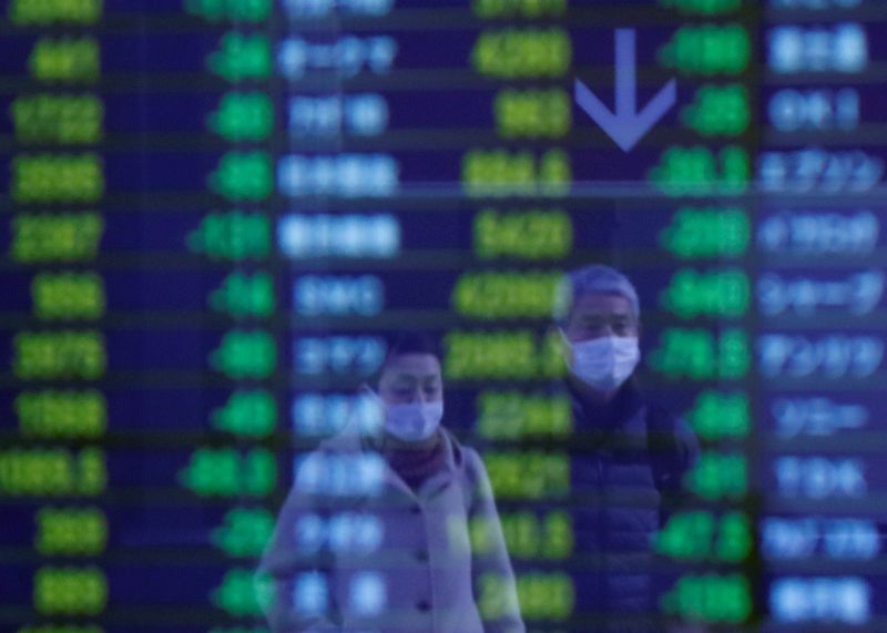 Passersby wearing protective face masks, following an outbreak of the coronavirus, are reflected on a screen displaying stock prices outside a brokerage in Tokyo