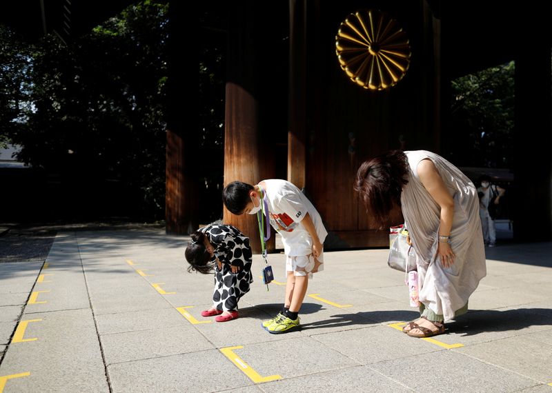 A family members weairng protective face masks bow their heads toward the main shrine as they visit to pay tribute to the war dead at Yasukuni Shrine, in Tokyo