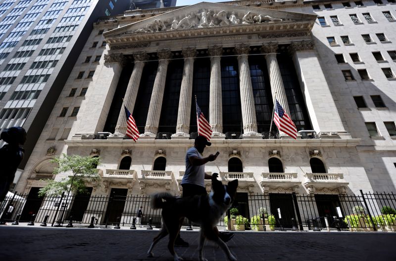 A man walks a dog in the shade past the New York Stock Exchange (NYSE) during hot weather in New York