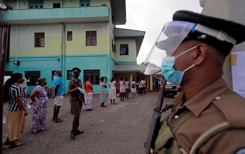 People wearing protective masks wait in a line to cast their vote outside a polling station during the country's parliamentary election in Colombo