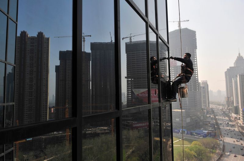 A labourer cleans the window of an office building near a residential complex under construction in Shenyang