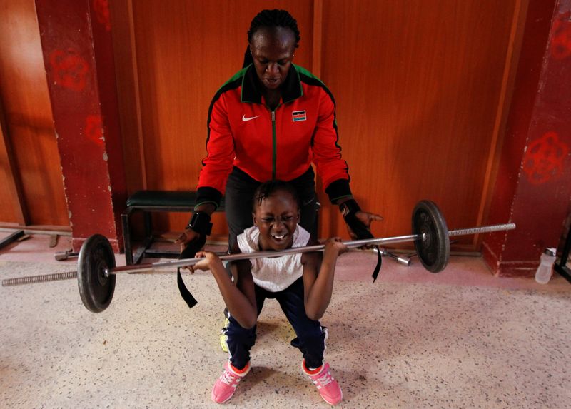 Kenyan weightlifter Mercy Obiero assists her granddaughter Keysha Atiky to lifts weights during a training session at a gym within Umoja estate in Nairobi