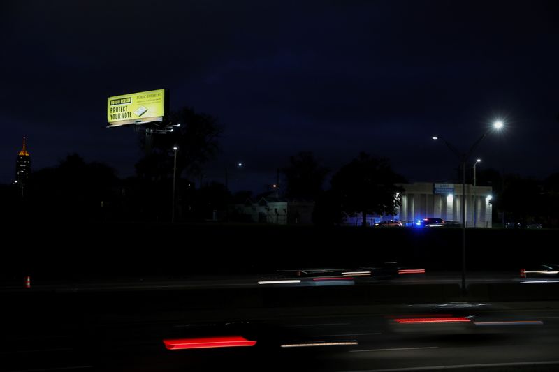 A billboard advertising to 'Vote In Person' is seen as a patrol car for the Detroit Police Department pulls a car over as traffic drives by in Detroit, Michigan