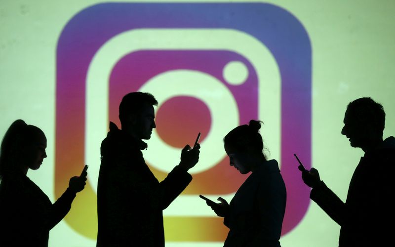 FILE PHOTO: Silhouettes of mobile users are seen next to a screen projection of the Instagram logo in this picture illustration