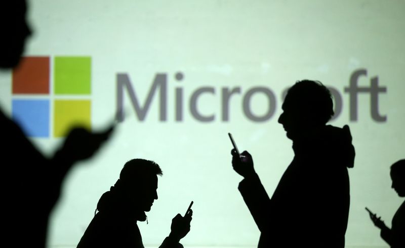 Silhouettes of mobile users are seen next to a screen projection of Microsoft logo in this picture illustration