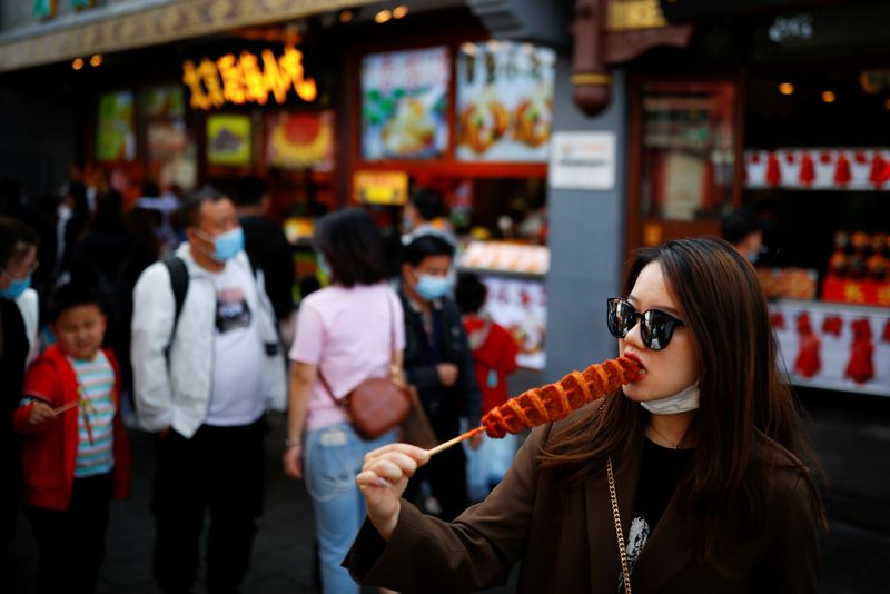 FILE PHOTO: A woman eats as people walk in the tourist area surrounding Houhai Lake during Chinese National Day holidays in Beijing