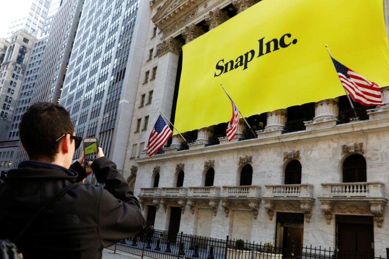 A man takes a photograph of the front of the New York Stock Exchange (NYSE) with a Snap Inc. logo hung on the front of it shortly before the company's IPO in New York