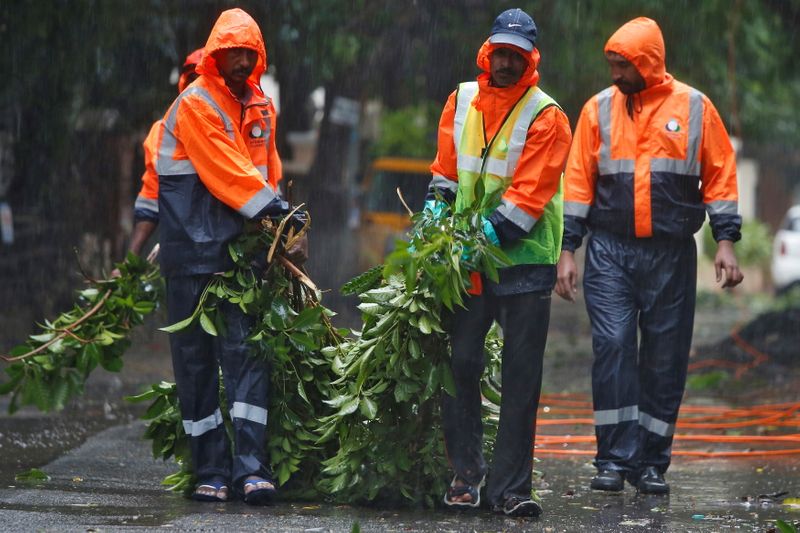 Municipal workers remove fallen tree branches from a road during rains before Cyclone Nivar's landfall, in Chennai