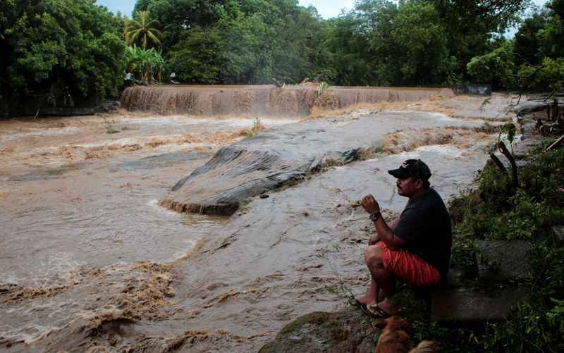 A man sits on the shore of the Masachapa river under the rain caused by Storm Eta in Masachapa