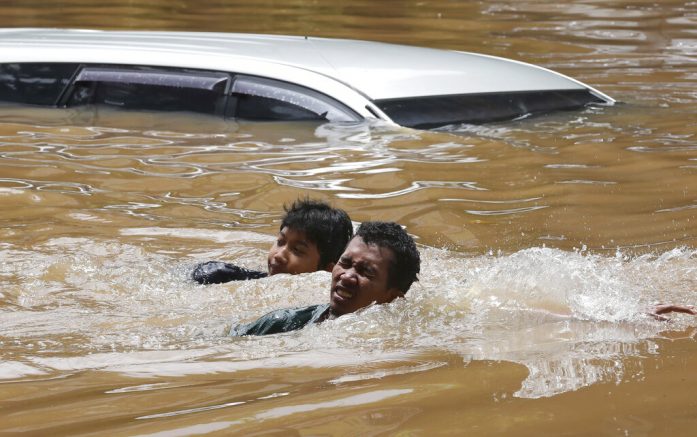 People swim through a flooded neighborhood following heavy rains in Jakarta, Indonesia, Saturday, Feb. 20, 2021. Heavy downpours combined with poor city sewage planning often causes heavy flooding in parts of greater Jakarta. (AP Photo/Tatan Syuflana)