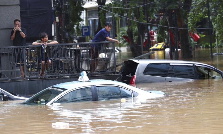 People stand above at an office yard flooded following heavy rains, Saturday, Feb. 20, 2021 in Jakarta, Indonesia. Heavy downpours combined with poor city sewage planning often causes heavy flooding in parts of greater Jakarta. (AP Photo/Tatan Syuflana)