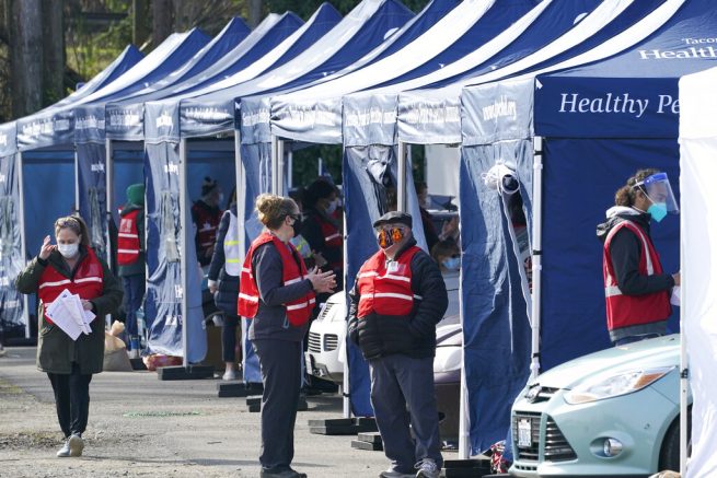 Workers stand near tents at a drive-up mass vaccination site, Thursday, March 4, 2021, in Puyallup, Wash., south of Seattle. Officials said they expected to deliver approximately 2500 second doses of the Moderna COVID-19 vaccine at the site Thursday. (AP Photo/Ted S. Warren)
