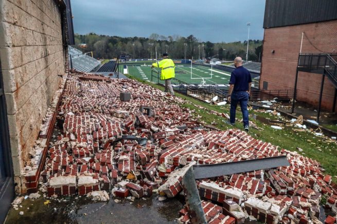 Newnan police officer Donald Evans, left, and principal Chase Puckett walk through the damaged campus of Newnan High School., Friday, March 26, 2022, in Newnan, Ga., the day after a dangerous tornado moved through the area, (John Spink/Atlanta Journal-Constitution via AP)