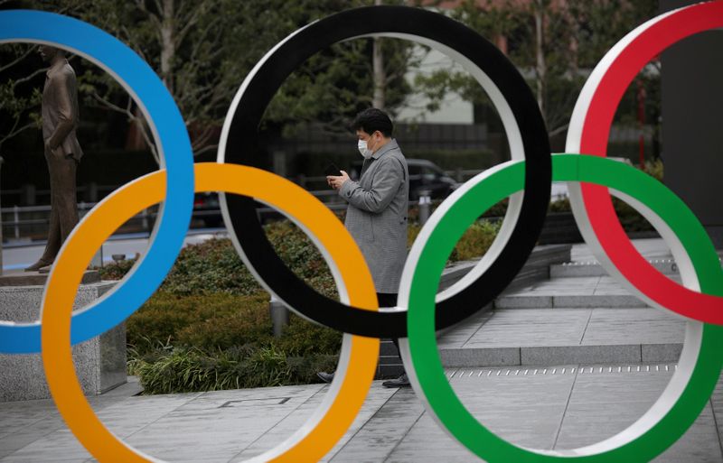 FILE PHOTO: Man looks at his mobile phone next to The Olympic rings in front of the Japan Olympics Museum in Tokyo
