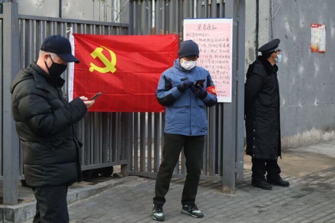 People wear protective face masks as they stand near a Communist Party flag at the entrance to a residential compound in Beijing on February 9, 2020. - The death toll from the novel coronavirus surged past 800 in mainland China on February 9, overtaking global fatalities in the 2002-03 SARS epidemic, even as the World Health Organization said the outbreak appeared to be stabilising. (Photo by GREG BAKER / AFP) (Photo by GREG BAKER/AFP via Getty Images)