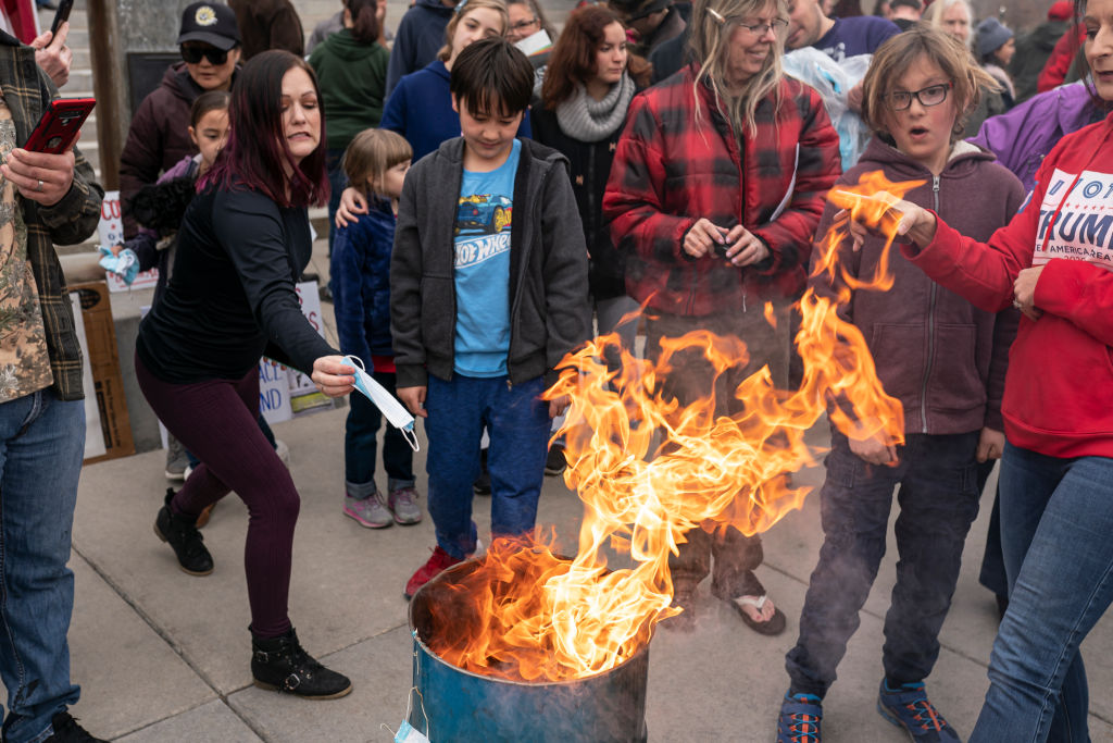 BOISE, ID - MARCH 06: A protester tosses a surgical mask into the fire during a mask burning event at the Idaho Statehouse on March 6, 2021 in Boise, Idaho. Citizens and politicians, including the Lieutenant Governor Janice McGeachin, gathered in at least 20 cities across the state to protest COVID-19 restrictions. (Photo by Nathan Howard/Getty Images)