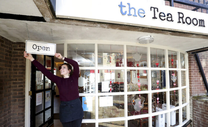 Harriet Henry, manager of The Tea Room in Knutsford, England, poses with the Open sign outside her cafe, as she prepares to open, Sunday April 11, 2021. Millions of people in Britain will get their first chance in months for haircuts, casual shopping and restaurant meals on Monday, as the government takes the next step on its lockdown-lifting roadmap. (Martin Rickett/PA via AP)