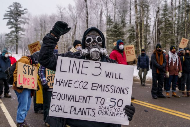 A Native American environmental activist holds a sign in front of the construction site for the Line 3 oil pipeline site near Palisade, Minnesota on January 9, 2021. - Line 3 is an oil sands pipeline which runs from Hardisty, Alberta, Canada to Superior, Wisconsin in the United States. In 2014, a new route for the Line 3 pipeline was proposed to allow an increased volume of oil to be transported daily. While that project has been approved in Canada, Wisconsin, and North Dakota, it has sparked continued resistance from climate justice groups and Native American communities in Minnesota. While many people are concerned about potential oil spills along Line 3, some Native American communities in Minnesota have opposed the project on the basis of treaty rights. (Photo by Kerem Yucel / AFP) (Photo by KEREM YUCEL/AFP via Getty Images)