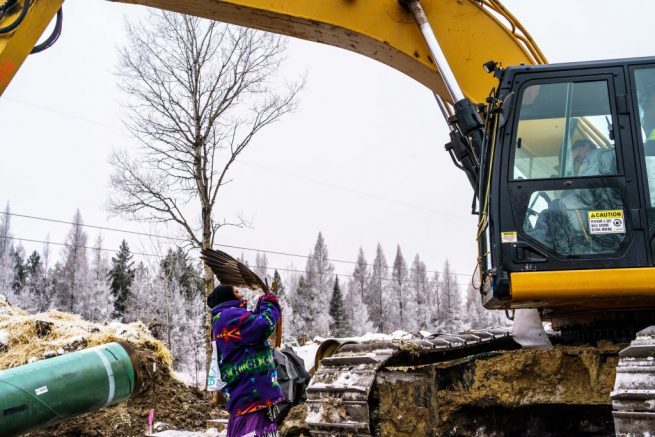 A Native American environmental activist shows an eagle feather to a construction worker in a bulldozer at the construction site for the Line 3 oil pipeline near Palisade, Minnesota on January 9, 2021. - Line 3 is an oil sands pipeline which runs from Hardisty, Alberta, Canada to Superior, Wisconsin in the United States. In 2014, a new route for the Line 3 pipeline was proposed to allow an increased volume of oil to be transported daily. While that project has been approved in Canada, Wisconsin, and North Dakota, it has sparked continued resistance from climate justice groups and Native American communities in Minnesota. While many people are concerned about potential oil spills along Line 3, some Native American communities in Minnesota have opposed the project on the basis of treaty rights. (Photo by Kerem Yucel / AFP) (Photo by KEREM YUCEL/AFP via Getty Images)