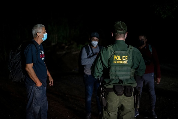 An agent with Border Patrol speaks to a group of migrant men after being apprehended near the border between Mexico and the United States in Del Rio, Texas on May 16, 2021. - Crossings in Del Rio have risen significantly this year with many crossings earlier this year by Haitian migrants and now many coming to seek asylum from Venezuela. (Photo by Sergio FLORES / AFP) (Photo by SERGIO FLORES/AFP via Getty Images)
