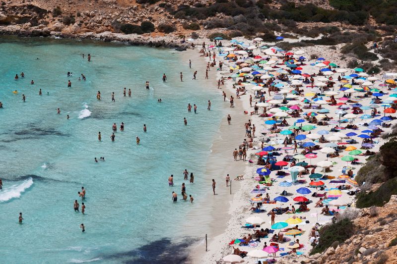 FILE PHOTO: People sunbathe on the beach on the Sicilian island of Lampedusa, as a flow of migrants arriving on the Mediterranean island, in Lampedusa, Italy, June 22, 2021.