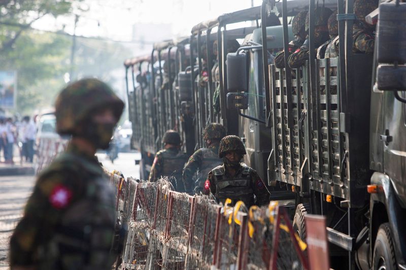 FILE PHOTO: Soldiers stand next to military vehicles as people gather to protest against the military coup, in Yangon