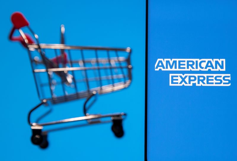 Smartphone with American Express logo is placed near toy shopping cart in this illustration