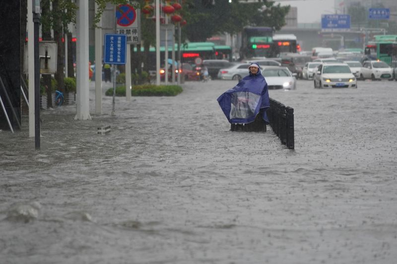 Resident wearing a rain cover stands on a flooded road in Zhengzhou, Henan province