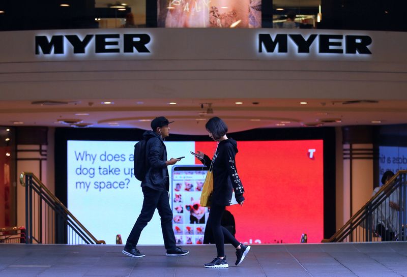 Shoppers use their phones as they walk past the entrance to a Myer department store in Sydney