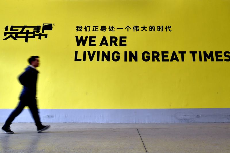 FILE PHOTO: A man walks past a sign of Huochebang or Truck Alliance, an app for truck services, in Guiyang