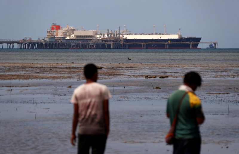 FILE PHOTO: Locals walk along small beach where LNG carrier called Kumul is docked at marine facility of ExxonMobil PNG Limited operated LNG plant at Caution Bay, located on outskirts of Port Moresby