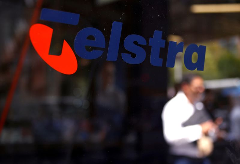 FILE PHOTO: A man looks at his phone as he walks past a Telstra logo adorning a phone booth in the central business district of Sydney