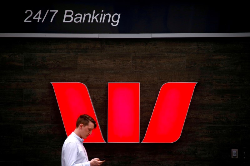 FILE PHOTO: FILE PHOTO: A pedestrian looks at his phone as he walks past a logo for Australia's Westpac Banking Corp located outside a branch in central Sydney