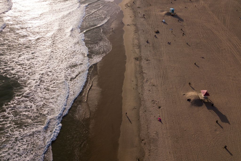 In this aerial image, people sit on the sand near the Huntington Beach pier before sunset on May 19, 2021 in Huntington Beach, California. - Orange County is now in the state's least-restrictive yellow tier of reopening. (Photo by Patrick T. FALLON / AFP) (Photo by PATRICK T. FALLON/AFP via Getty Images)